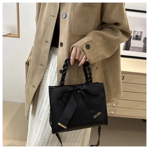 Close-up of elegant black handbag with satin bow and woven handle detail on a model