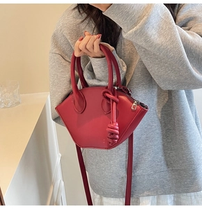 Détail du sac à main rouge en forme de coquille avec poignées cylindriques et fini mat