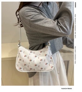 Close-up of a white half-moon shoulder bag with colorful floral prints and logo details