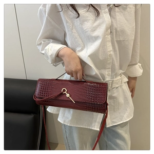 Detail of burgundy crocodile pattern baguette bag featuring gold key lock and long strap