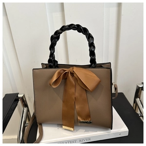 Close-up of brown handbag featuring a black woven handle and a large ribbon bow decoration
