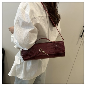 Detail of burgundy crocodile pattern baguette bag with golden key clasp on shoulder