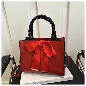 Detail of red bridal handbag with large bow, black woven handle and gold accents