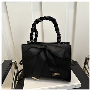 Detail of black leather handbag with braided handle and silk ribbon bow decoration