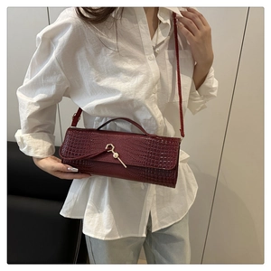 Detail of red crocodile texture handbag with gold buckle held by model in white shirt