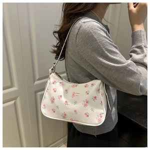 Détail du sac hobo blanc avec motifs floraux roses et nœud porté sur le côté par le modèle