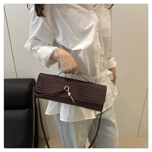 Detail of dark brown crocodile pattern handbag with gold clasp worn by a model