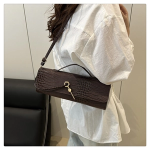 Detail of a dark brown crocodile embossed baguette bag with a gold hexagonal buckle clasp