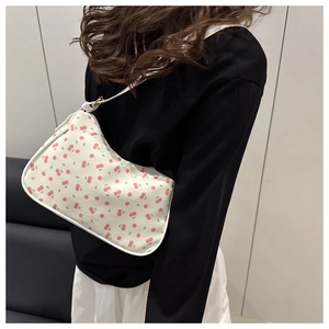 Close-up of a white crescent shoulder bag featuring red cherry prints worn by a model