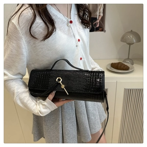 Detail of black faux crocodile leather baguette bag featuring a gold hexagonal metal buckle