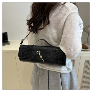 Detail of black faux crocodile leather baguette bag with luxury gold lock on white outfit