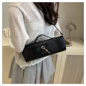 Detail of black crocodile texture baguette bag with golden hexagonal buckle and strap