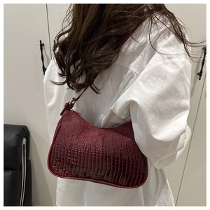 Side view of dark red crescent shoulder bag with glossy crocodile texture on white shirt