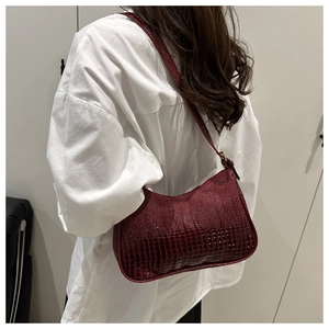 Detail view of burgundy faux crocodile leather shoulder bag on a white shirt
