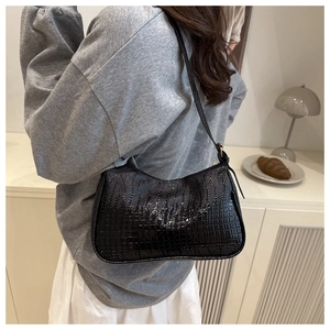 Detail of black crocodile texture baguette bag shown on shoulder in lifestyle setting