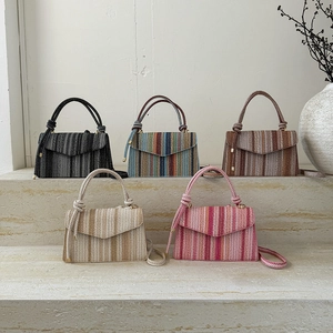 Mini sacs bandoulière en paille rayée en cinq couleurs sur un présentoir en pierre