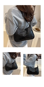 Detail of black faux leather underarm bag with crocodile pattern and golden hardware