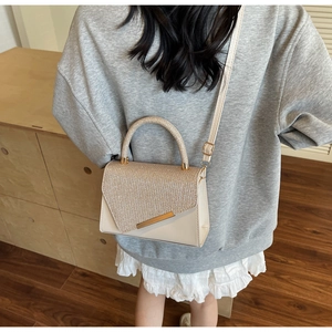 Detail of glitter flap handbag with gold metal accents worn by a model in a home setting