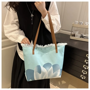 Detalle del bolso tote de lona azul claro con estampado floral y bordes deshilachados