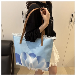 Detalle del bolso tote tie-dye azul con bordes deshilachados y correas de cuero marrón