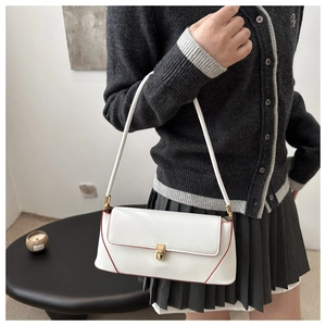 White baguette shoulder bag with red trim and gold lock worn by a model in gray outfit