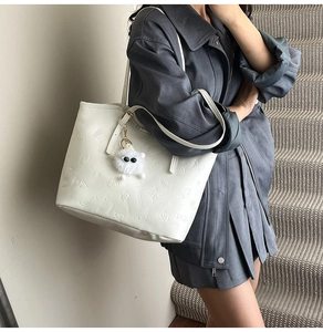 Detail of off-white leather tote bag with embossed letters and plush ball charm