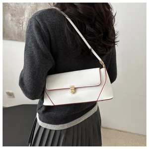 Close-up of white glossy baguette bag with red edges and gold buckle on a model