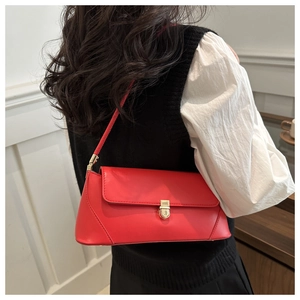 Detailed view of a vibrant red baguette shoulder bag worn by a model against a white wall