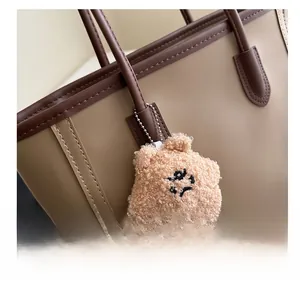 Close-up of a plush bear charm with silver chain on a beige leather tote handle