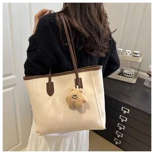 Close-up of a large beige tote bag with brown trim and a plush star pendant accessory