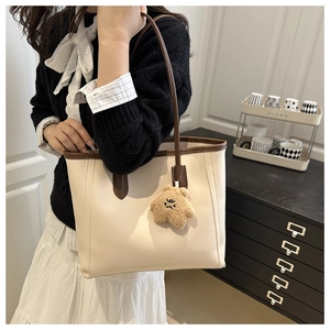 Detail of minimalist cream tote bag with brown straps and cute bear charm ornament