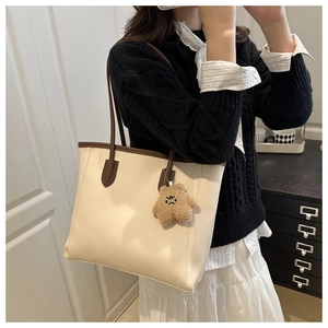 Detail of cream tote bag with dark brown contrast handles and a cute teddy bear charm