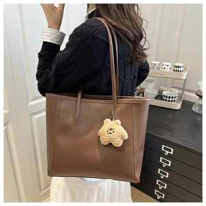 Detail of a brown leather tote bag with a yellow star plush charm on the shoulder