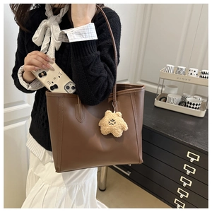 Detail of dark brown tote bag with yellow star plush charm and long shoulder straps