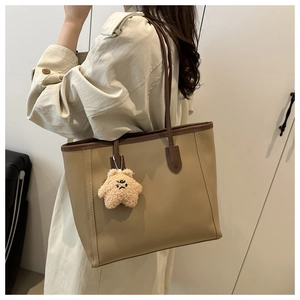 Detail of khaki tote bag with brown straps and a yellow plush star charm hanging on it