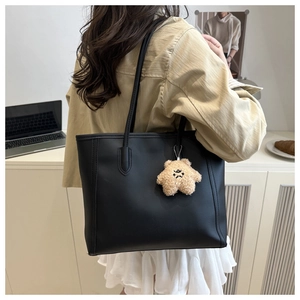 Minimalist black tote bag with plush star charm shown in a cozy office setting