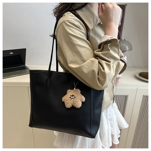 Close-up of black matte tote bag featuring a cute brown plush bear charm and slender straps