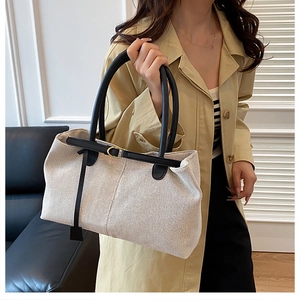 Close-up of beige tweed tote bag with black leather straps and gold buckle detail