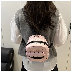 Rear view of a mini pink backpack with black swallow patterns and gold logo hardware