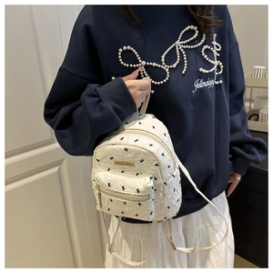 Detail of cream mini backpack featuring embossed patterns and gold Fashion logo plaque
