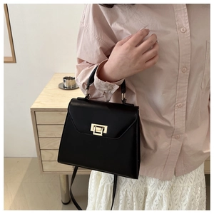 Close-up of a stylish black leather crossbody bag with golden clasp worn by a model