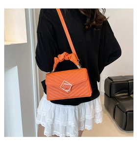 Orange pleated handbag with V-quilt stitching and square lock shown from a side back view