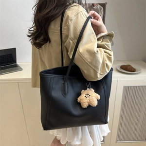 Large black matte tote bag with star plush charm shown on model in a modern office style