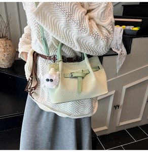 Detail of light green woven handbag featuring a furry charm and adjustable shoulder strap