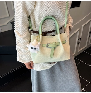 Detail of light green PU leather handbag with woven texture and white plush charm