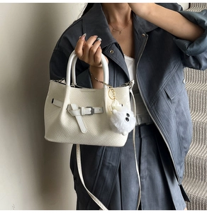 Detail of white woven texture handbag with buckle strap and plush charm on long coat