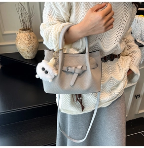 Detail of light grey woven texture handbag with belt buckle and plush charm decoration