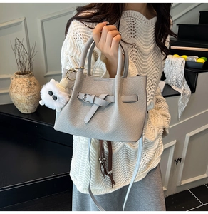 Light grey woven handbag with belt buckle detail and plush charm on a model