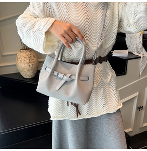Detail of light gray woven texture handbag with decorative belt buckle shown on model