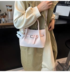 Detail of light pink woven handbag with belt buckle and cute plush cartoon keychain